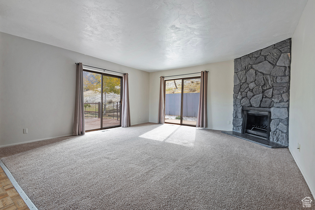 Unfurnished living room featuring carpet, a textured ceiling, a fireplace, and a healthy amount of sunlight