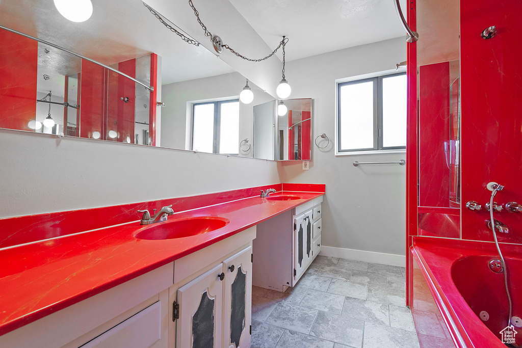 Full bathroom with double vanity, baseboards, a washtub, and a sink