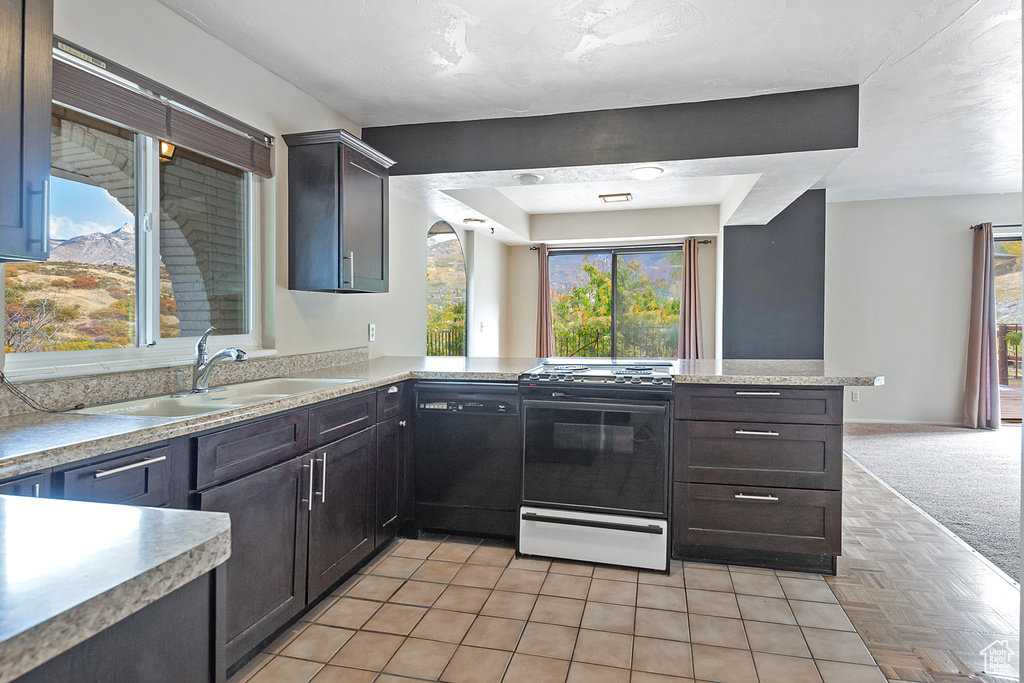 Kitchen with black dishwasher, a peninsula, gas range oven, light countertops, and a sink