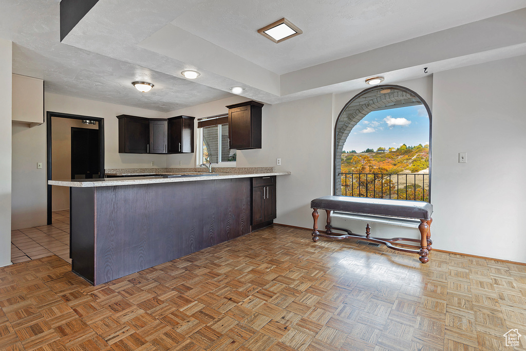 Kitchen featuring a peninsula, dark brown cabinetry, light countertops, and a textured ceiling