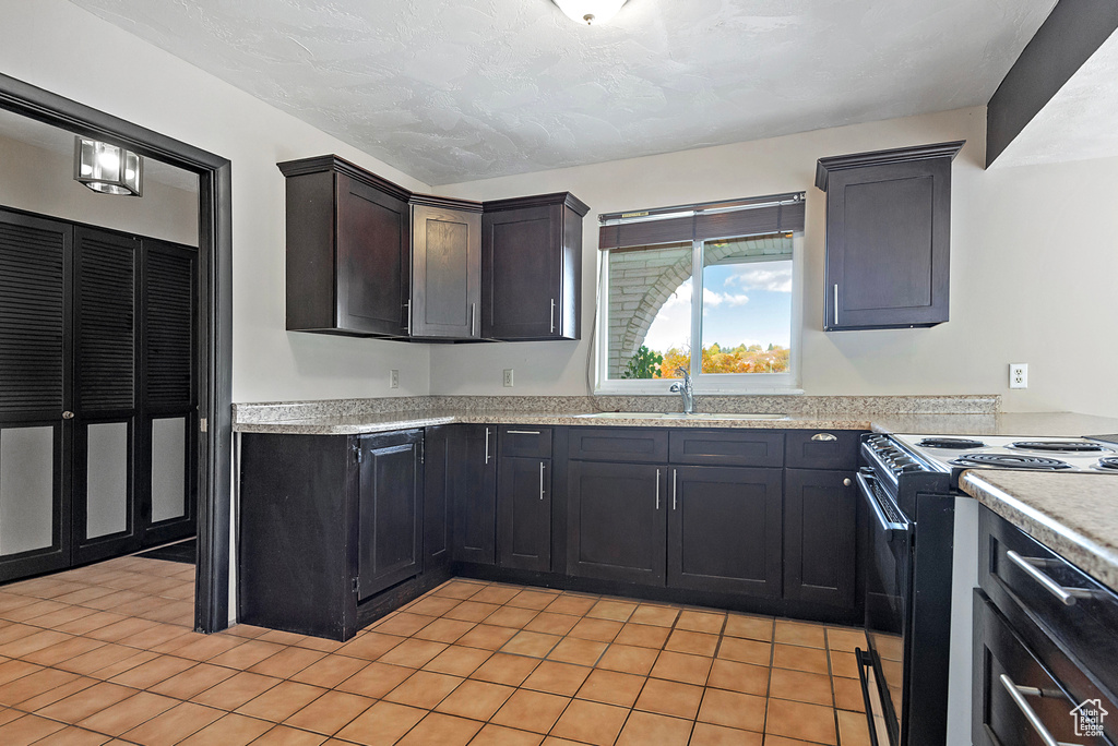 Kitchen featuring light tile patterned floors, electric range, light countertops, a textured ceiling, and a sink