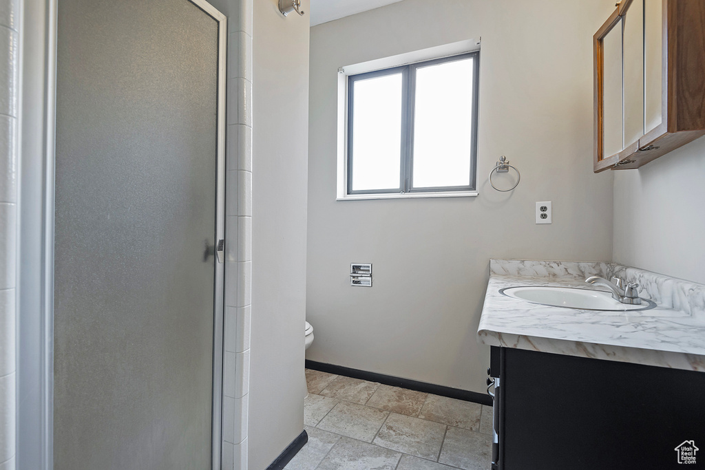 Full bath featuring toilet, a stall shower, stone finish flooring, vanity, and baseboards