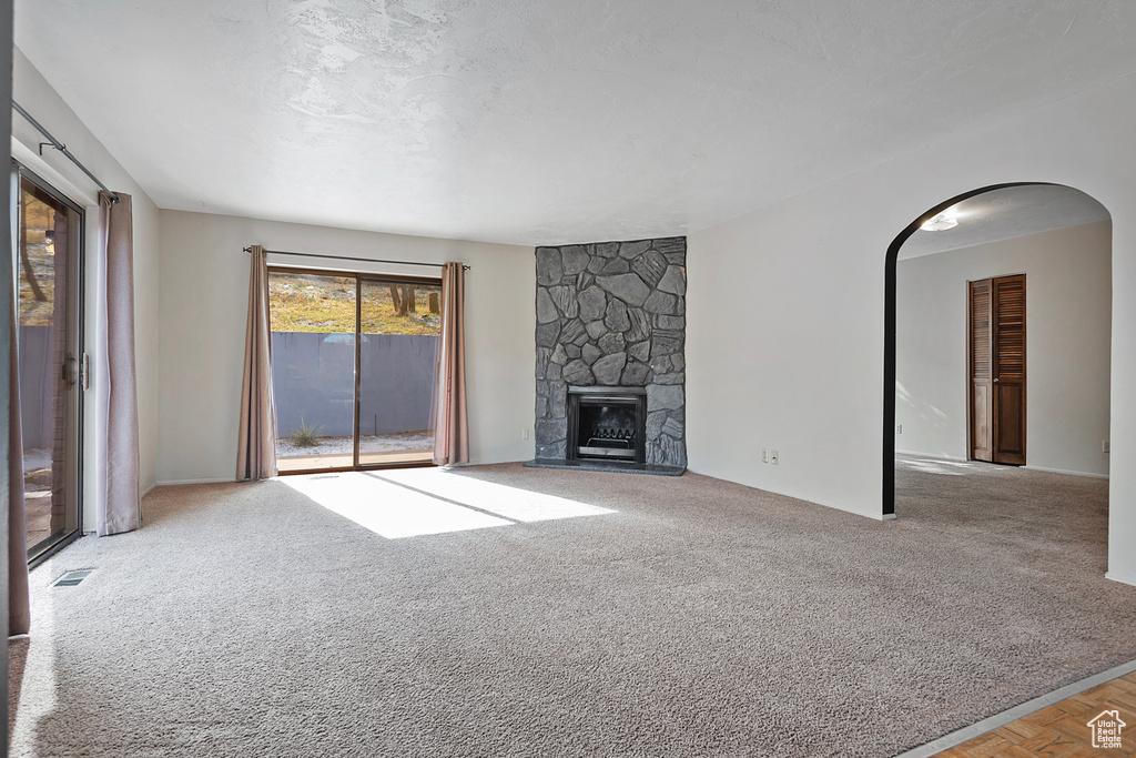 Unfurnished living room with arched walkways, a fireplace, carpet flooring, and visible vents