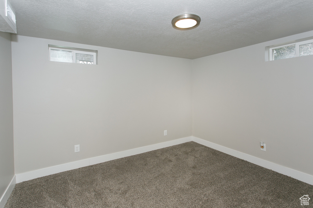 Basement featuring baseboards, dark colored carpet, and a textured ceiling