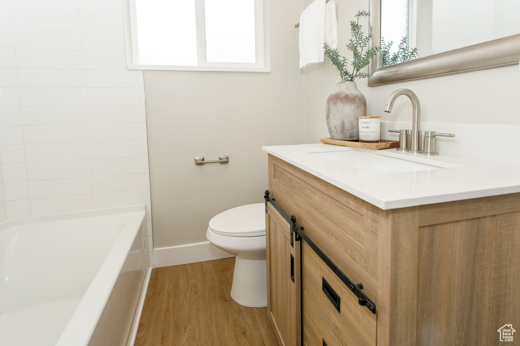 Full bathroom with vanity, wood finished floors, toilet, and a healthy amount of sunlight