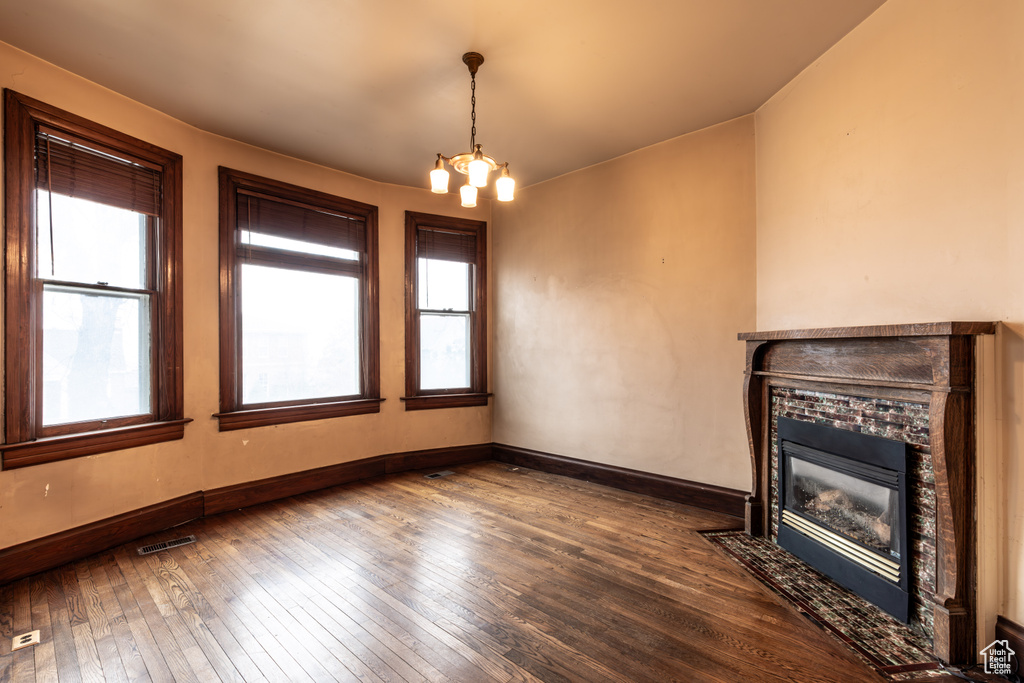 Unfurnished living room featuring a notable chandelier, a fireplace with flush hearth, visible vents, baseboards, and dark wood finished floors