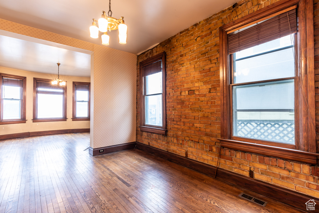 Unfurnished room featuring a notable chandelier, dark wood-style flooring, visible vents, baseboards, and wallpapered walls