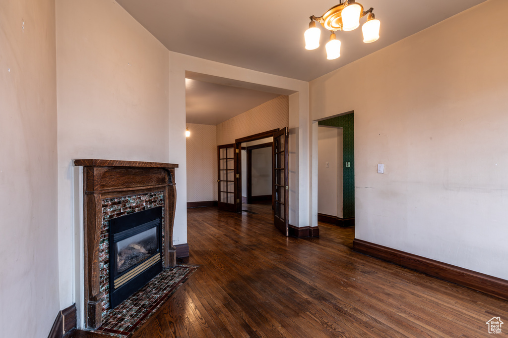 Unfurnished living room featuring dark wood-style floors, a notable chandelier, a tile fireplace, and baseboards