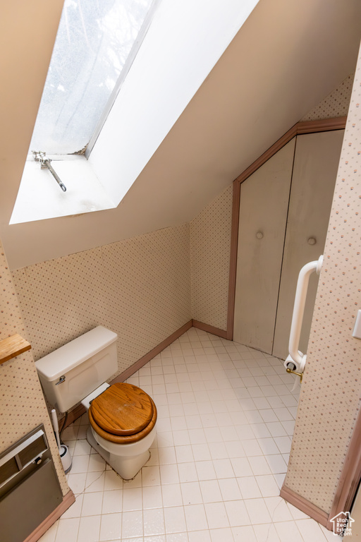 Bathroom with toilet, wallpapered walls, tile patterned flooring, and lofted ceiling with skylight