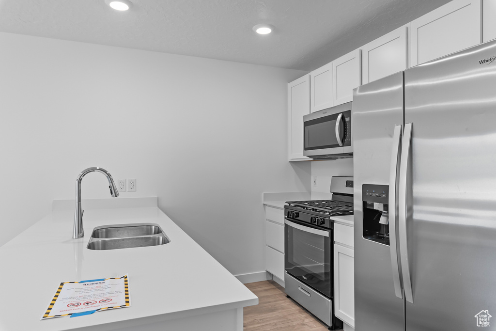 Kitchen with light wood finished floors, stainless steel appliances, light countertops, white cabinets, and a sink