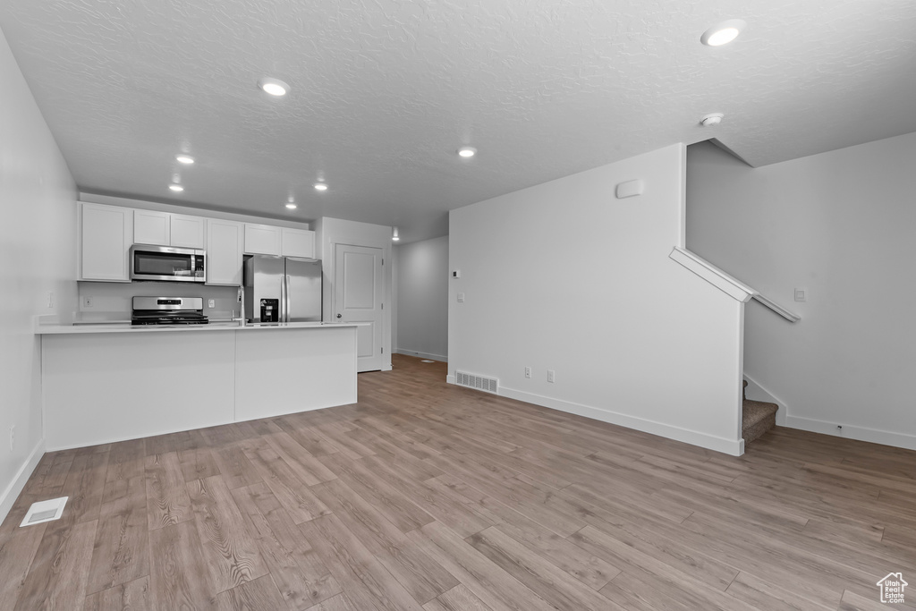 Kitchen with appliances with stainless steel finishes, visible vents, light wood-style floors, and a peninsula
