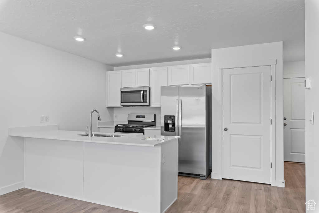 Kitchen with a peninsula, light wood finished floors, appliances with stainless steel finishes, and white cabinets