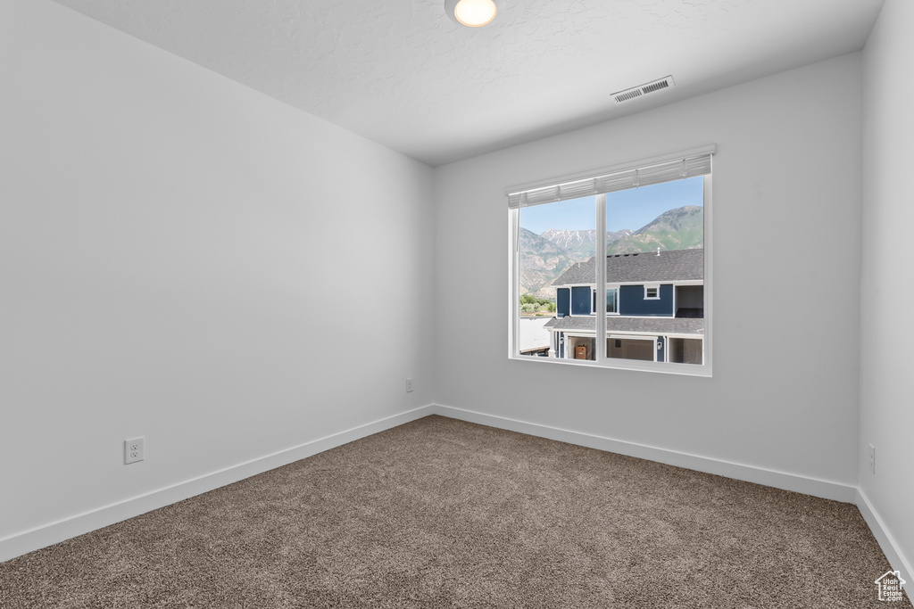 Empty room with a textured ceiling, carpet, visible vents, and baseboards