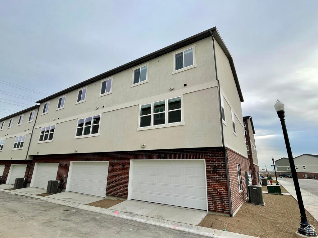 Rear view of property with stucco siding, brick siding, an attached garage, and central AC unit