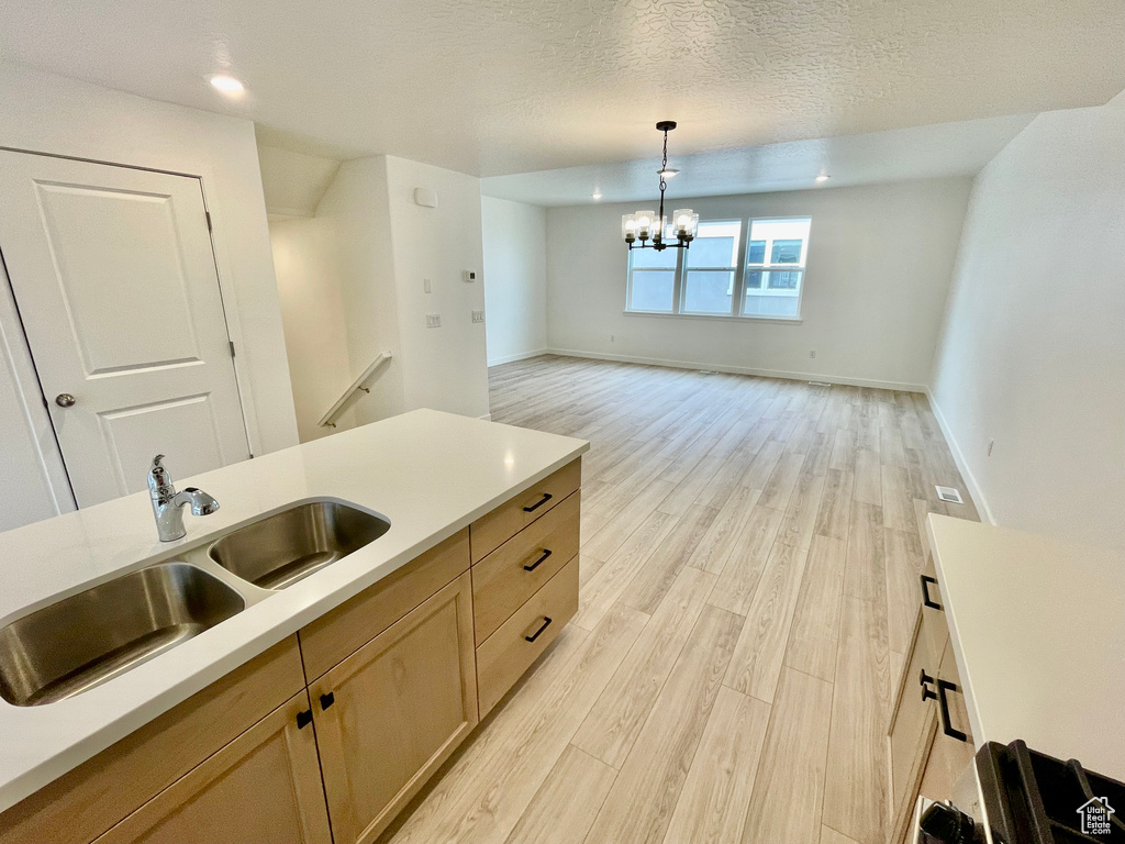Kitchen with pendant lighting, light wood-type flooring, a chandelier, light countertops, and a sink