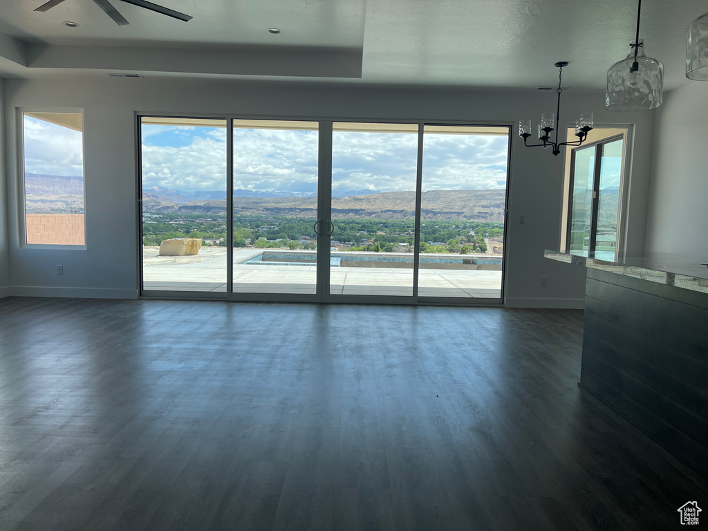 Unfurnished room with baseboards, a ceiling fan, dark wood finished floors, a chandelier, and a raised ceiling