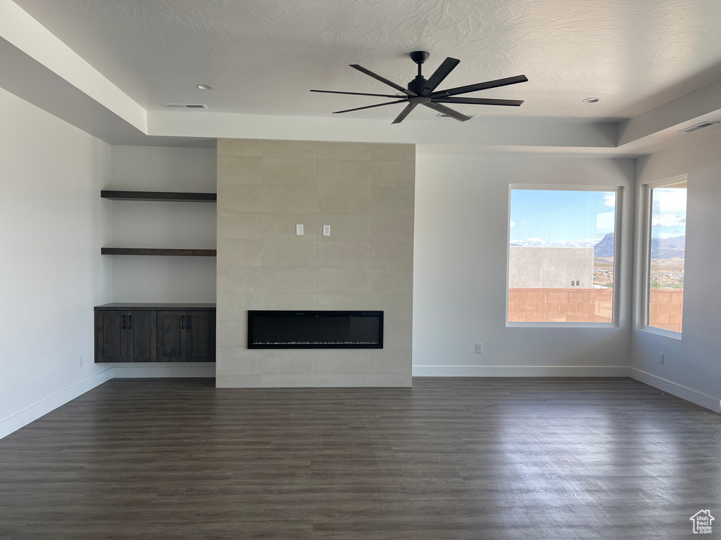 Unfurnished living room featuring dark wood-type flooring, baseboards, a ceiling fan, and a tiled fireplace
