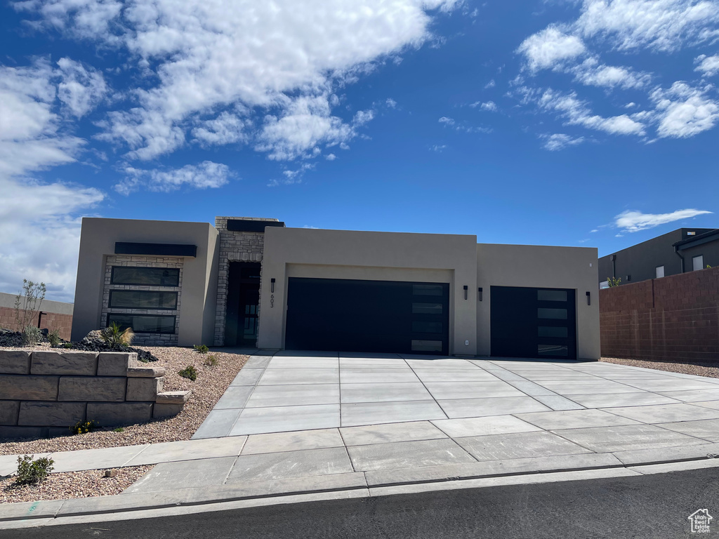 Contemporary home with stucco siding, an attached garage, driveway, and fence