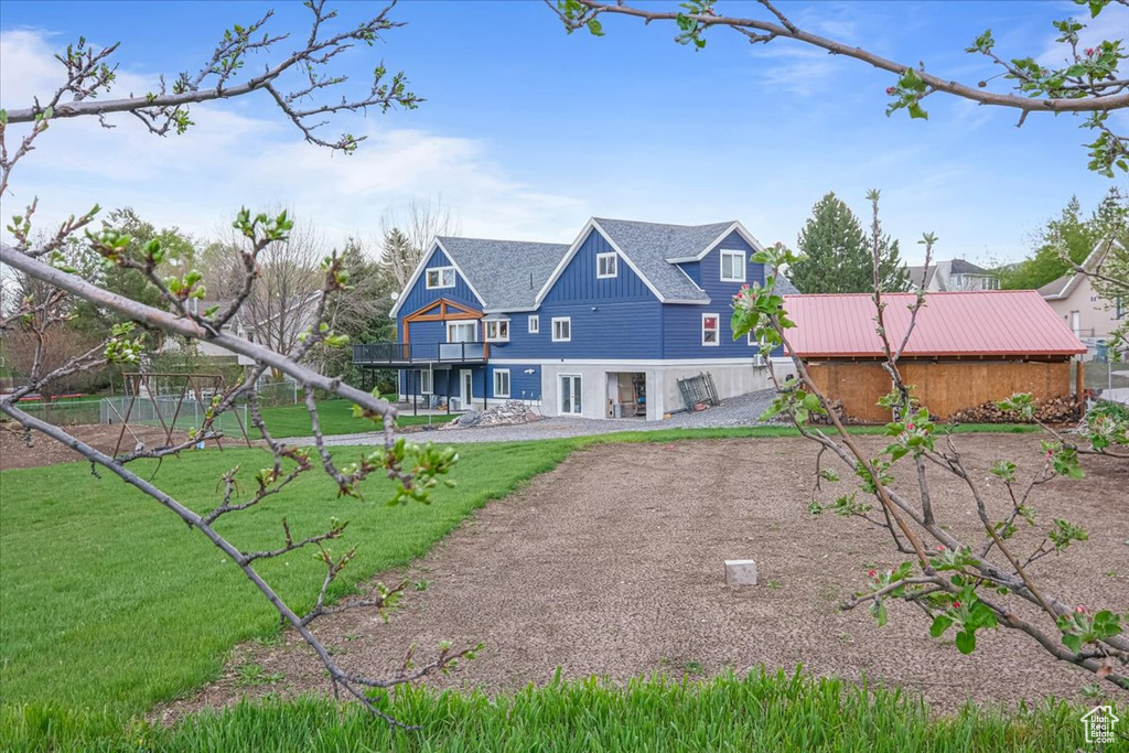 Back of house with a yard, board and batten siding, and a balcony