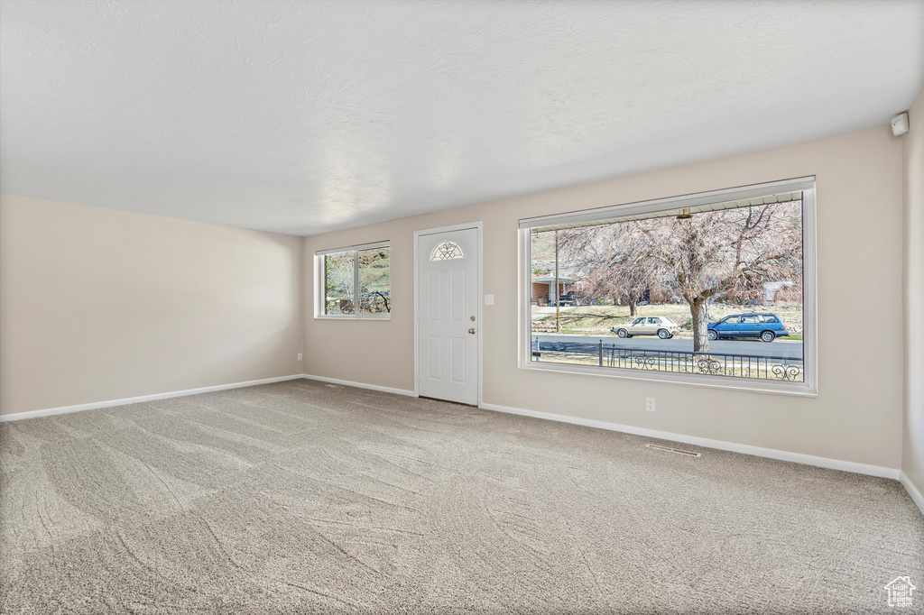 Carpeted spare room featuring a textured ceiling, visible vents, and baseboards