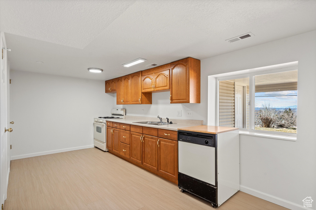 Kitchen with white appliances, a sink, visible vents, light wood-style floors, and light countertops