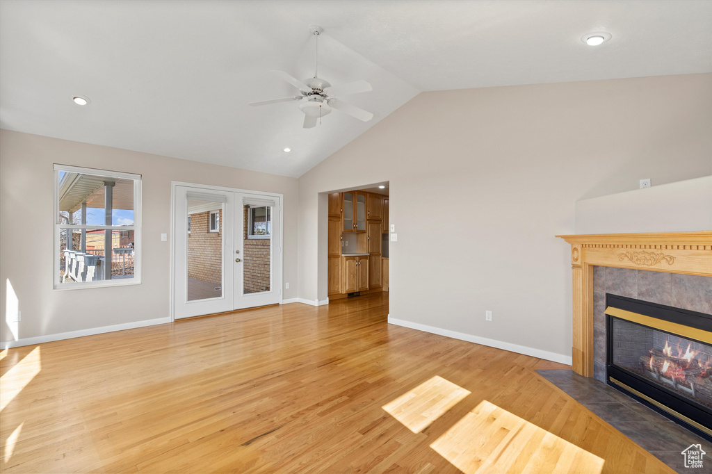 Unfurnished living room with french doors, lofted ceiling, light wood-style flooring, a high end fireplace, and baseboards