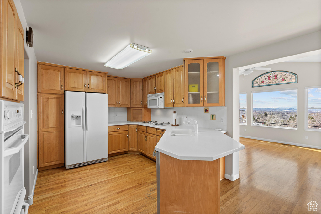 Kitchen featuring a peninsula, white appliances, a sink, light wood finished floors, and glass insert cabinets