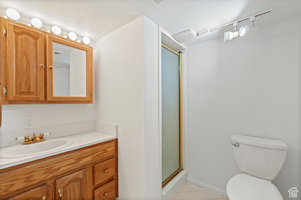 Full bathroom with a textured ceiling, toilet, vanity, baseboards, and a stall shower