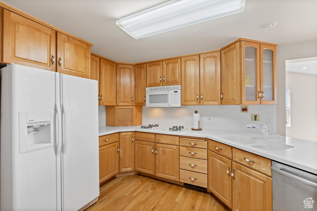 Kitchen with light countertops, glass insert cabinets, a sink, light wood-type flooring, and white appliances