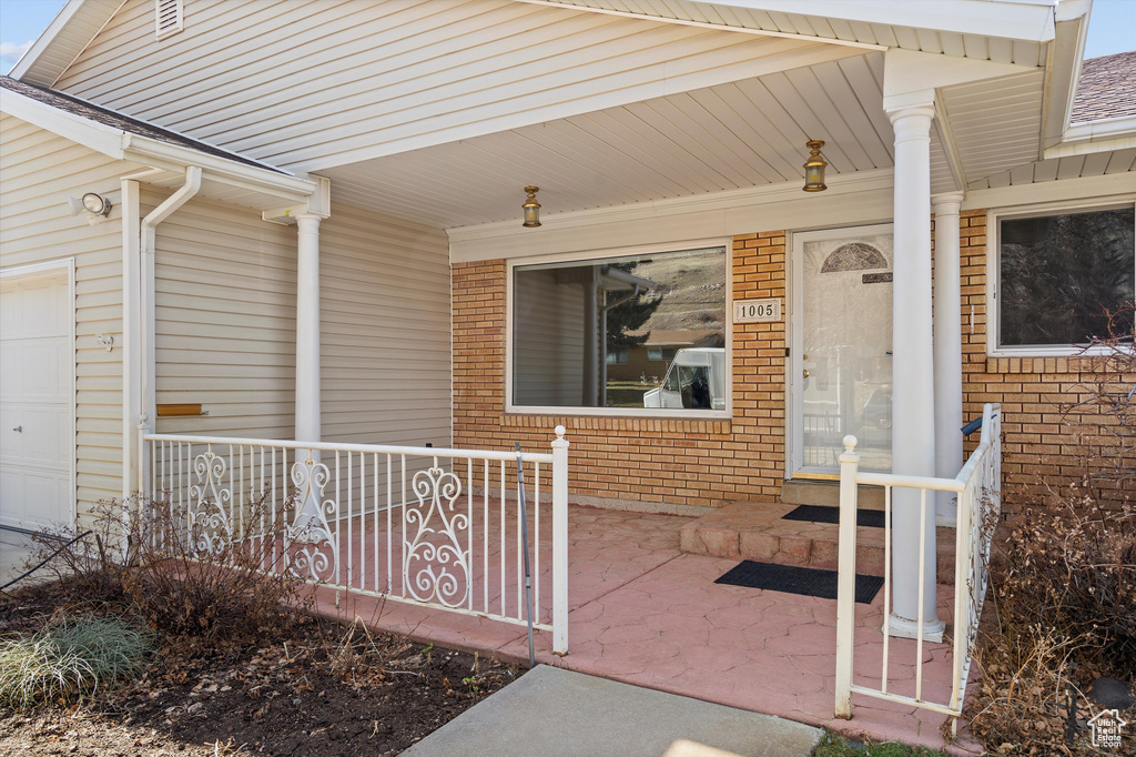 Entrance to property featuring a porch, brick siding, and a garage