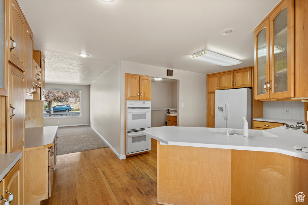 Kitchen with a peninsula, white appliances, a sink, light wood-type flooring, and glass insert cabinets