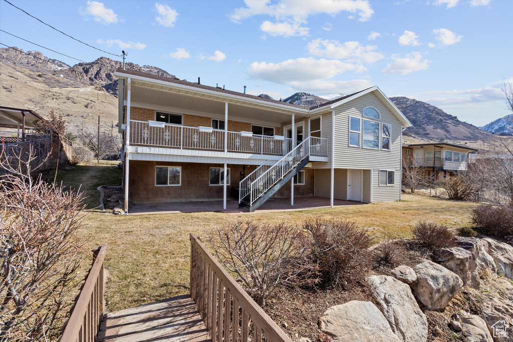 Back of house with stairs, a patio, a lawn, and a deck with mountain view