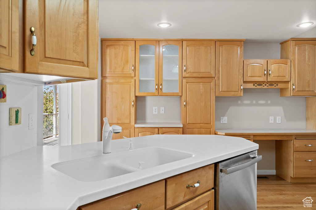 Kitchen featuring light wood finished floors, glass insert cabinets, a sink, light countertops, and stainless steel dishwasher