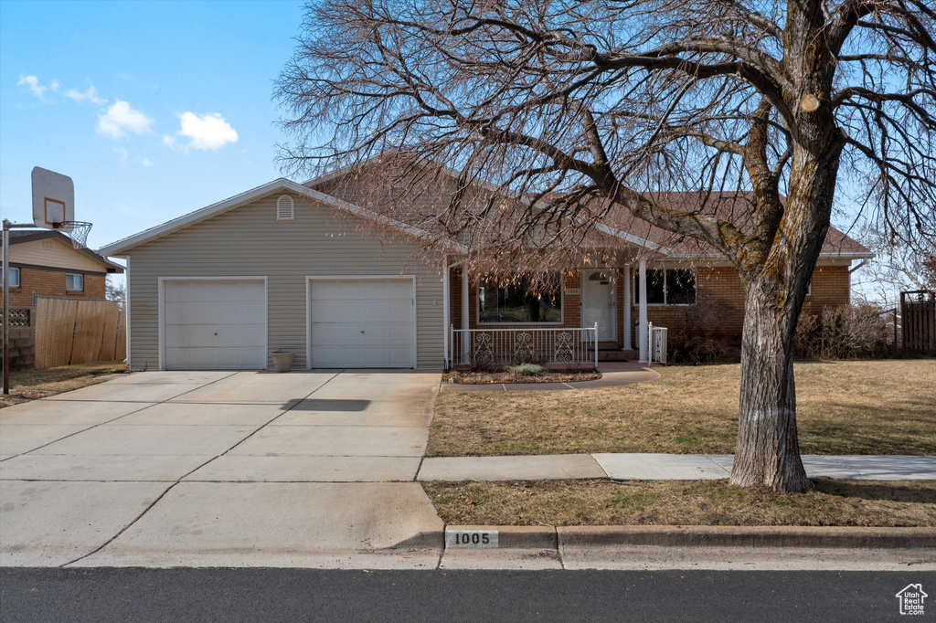 Ranch-style house with driveway, an attached garage, covered porch, fence, and a front lawn