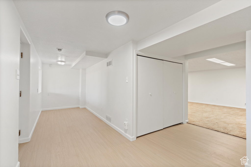 Finished basement with light wood-style floors, baseboards, and visible vents