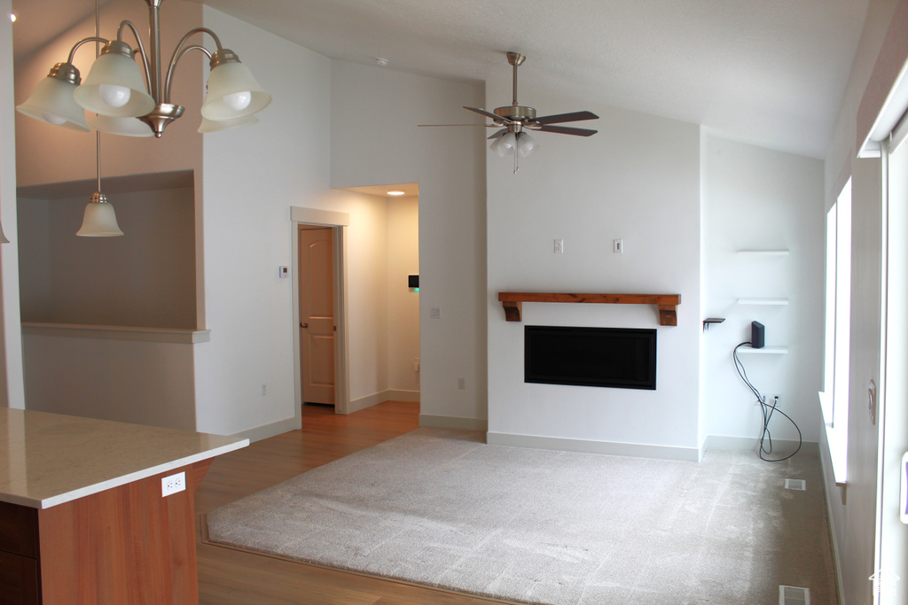 Unfurnished living room featuring a fireplace, light wood finished floors, ceiling fan, a chandelier, and high vaulted ceiling