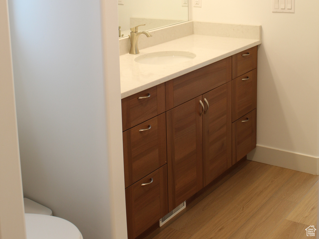 Bathroom featuring wood finished floors, vanity, baseboards, and toilet