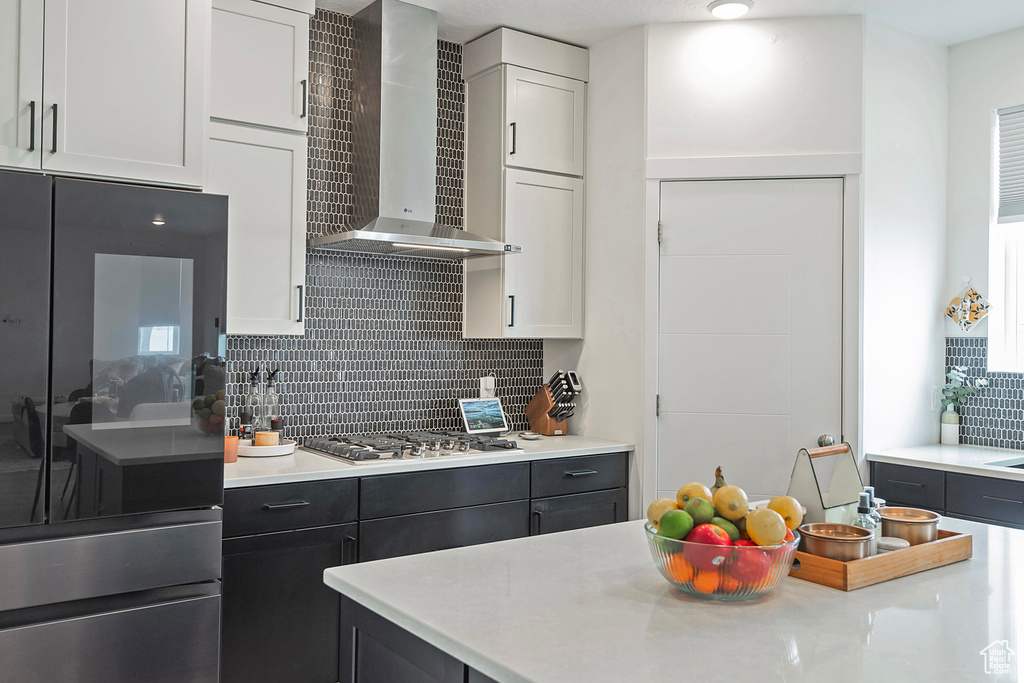 Kitchen with light countertops, stainless steel gas cooktop, and wall chimney range hood