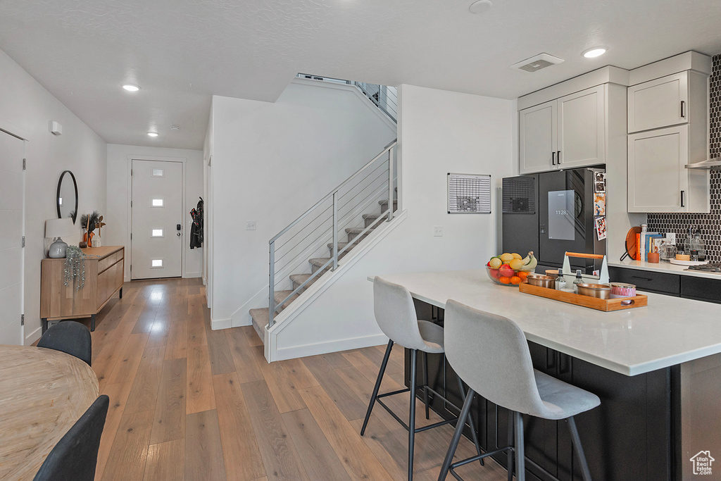 Kitchen with refrigerator, a breakfast bar, light countertops, white cabinetry, and light wood-type flooring