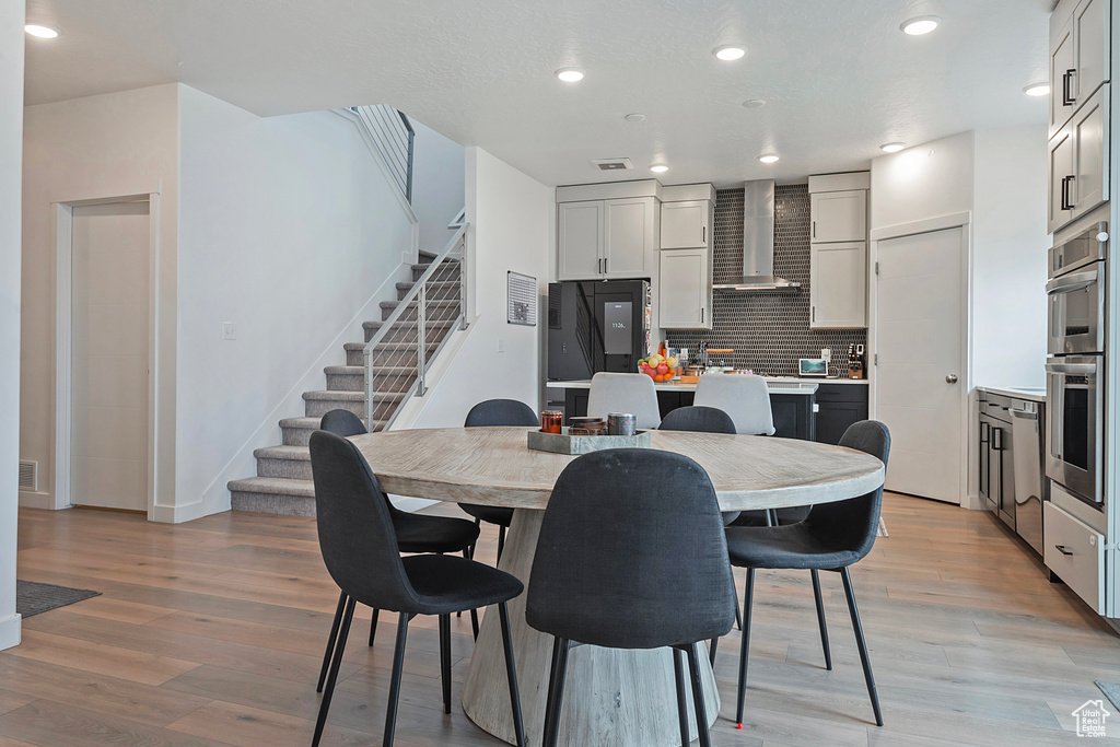 Kitchen with tasteful backsplash, double oven, light wood-type flooring, wall chimney exhaust hood, and fridge