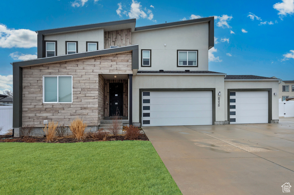 Contemporary house featuring stone siding, a front lawn, concrete driveway, and stucco siding