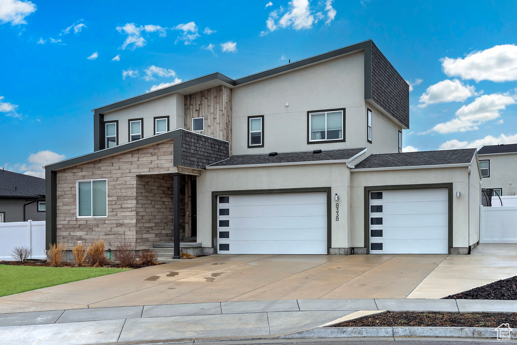 Contemporary home featuring an attached garage, driveway, stone siding, and fence