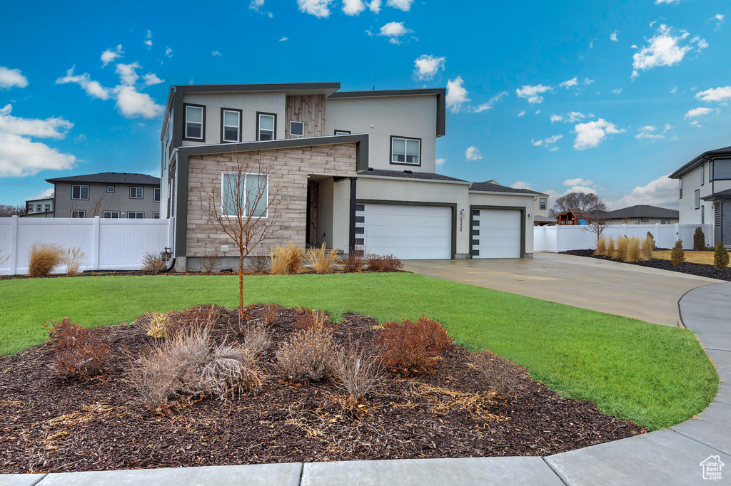 Modern home featuring stucco siding, an attached garage, fence, stone siding, and driveway