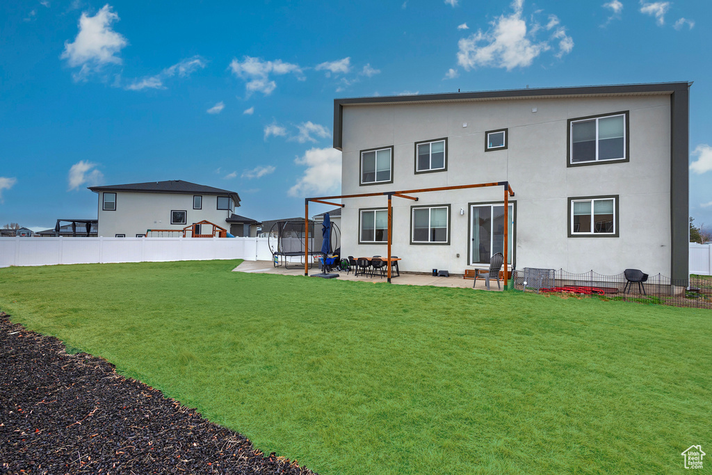 Back of property with fence, a yard, stucco siding, a trampoline, and a patio area