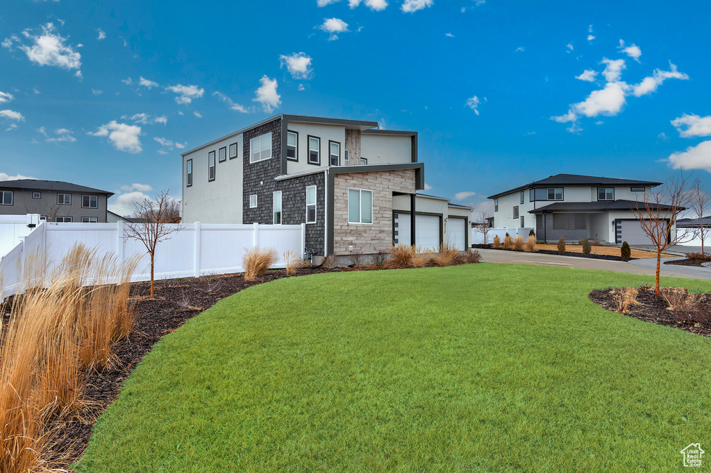 Back of property featuring stone siding, a lawn, an attached garage, and fence