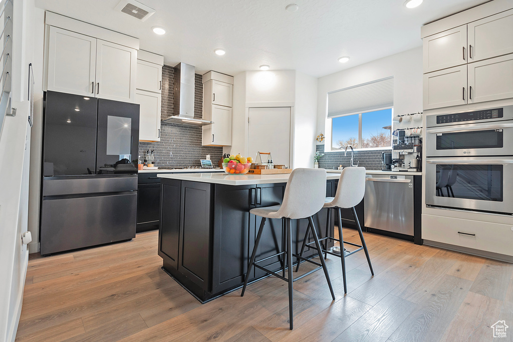 Kitchen featuring stainless steel appliances, wall chimney range hood, light countertops, and light wood-style floors