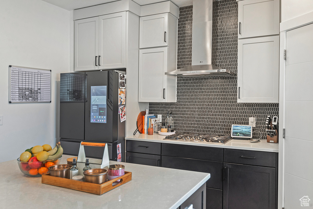 Kitchen featuring tasteful backsplash, wall chimney exhaust hood, light countertops, smart refrigerator, and stainless steel gas cooktop