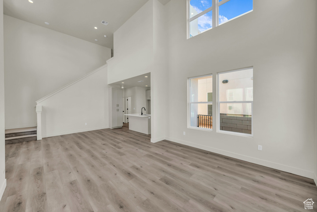 Unfurnished living room featuring recessed lighting, a sink, a towering ceiling, baseboards, and light wood-type flooring