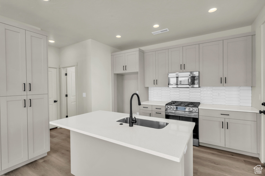 Kitchen with light wood finished floors, appliances with stainless steel finishes, a sink, backsplash, and recessed lighting