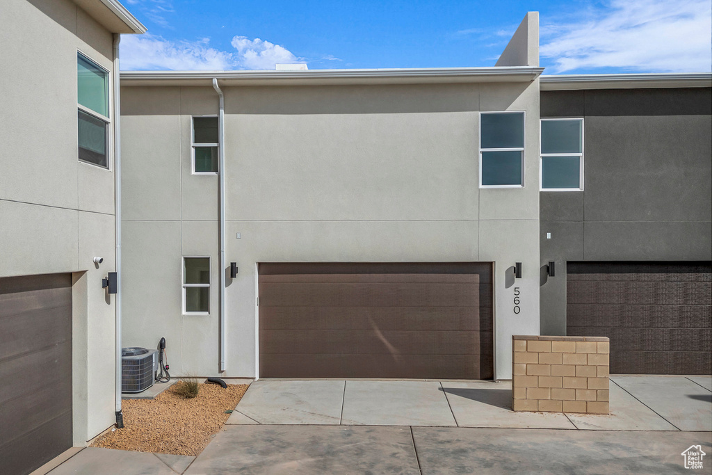 View of front facade featuring concrete driveway, stucco siding, an attached garage, and central AC unit